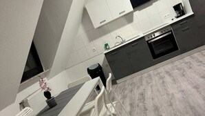 Une cuisine moderne avec des armoires blanches, une hotte noire et un four encastré. On y trouve une table à manger avec des chaises blanches et une petite plante en pot posée sur la table.