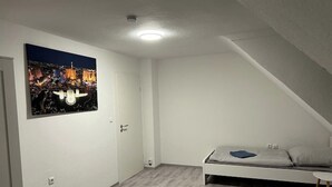 Une chambre à coucher avec un lit, une petite table de chevet et une commode. Il y a une porte et un interrupteur sur le mur.
