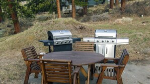 An outdoor dining area with a round table and wooden chairs, surrounded by two barbecue grills. - Fawn Valley Inn: 254 1 Bedroom Apts (Estes Park)