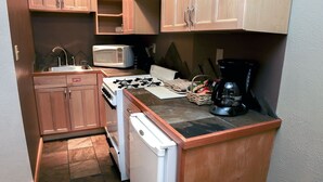 A compact kitchen with wooden cabinets, a microwave, a gas stove, a dishwasher, and a coffee maker. - Fawn Valley Inn: 254 1 Bedroom Apts (Estes Park)