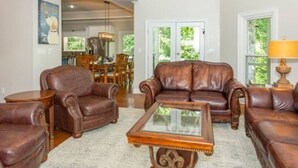 Uma sala de estar ampla com sofás de couro, uma mesa de centro de vidro e uma área de jantar ao fundo.