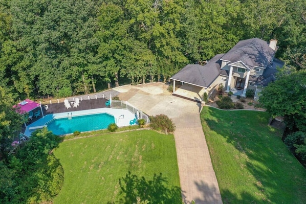 An aerial view of a residential property with a swimming pool, a covered patio, and a large lawn.