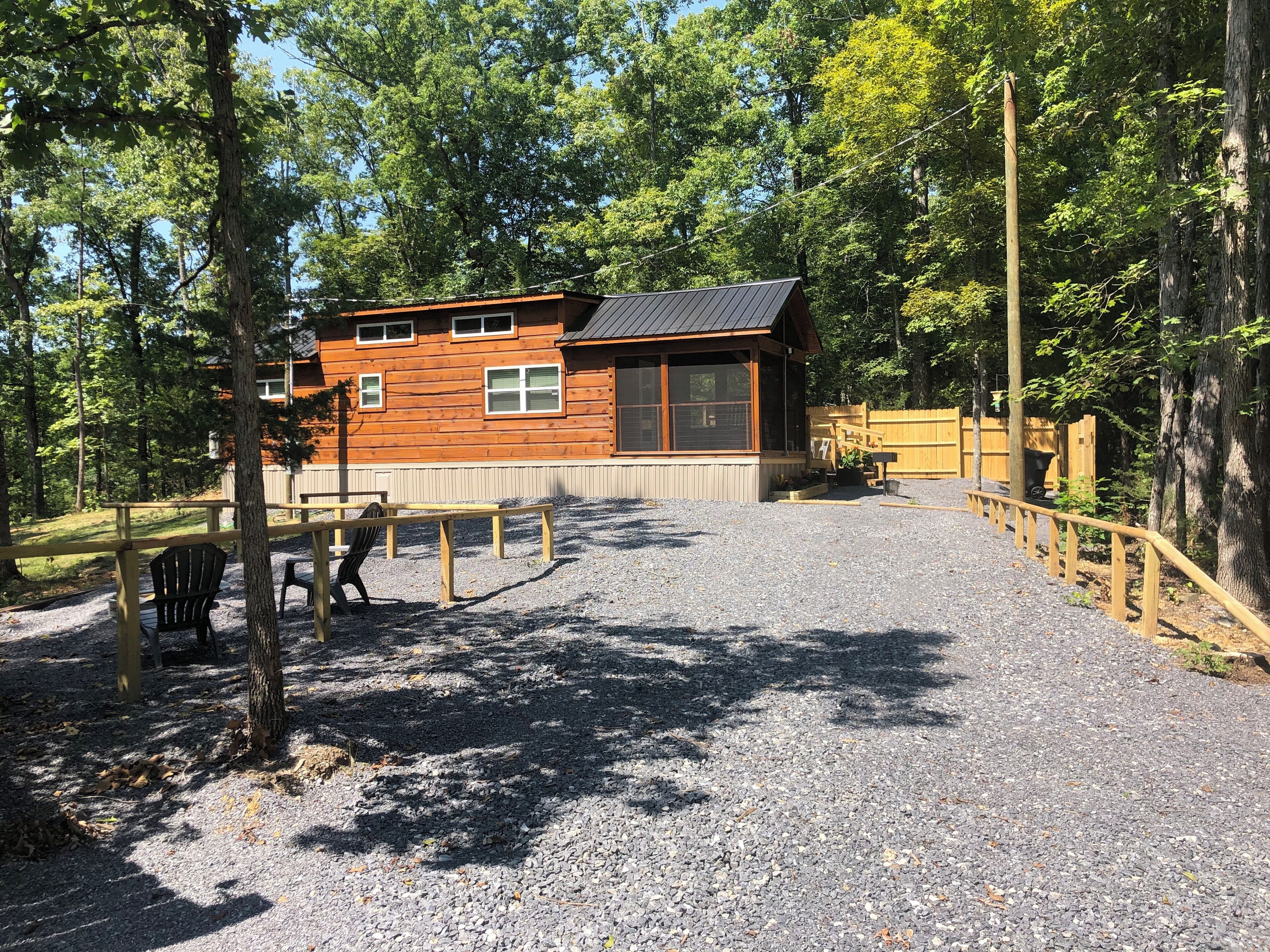 A wooden cabin with a gravel driveway and a wooden deck.