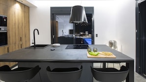 Et moderne køkken med en central ø, sorte stole og en hængende lampe.