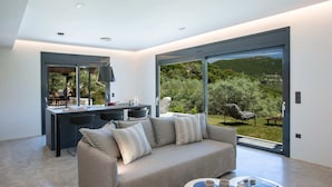 En moderne stue med sofa, spiseområde og en stor skydedør til en have.