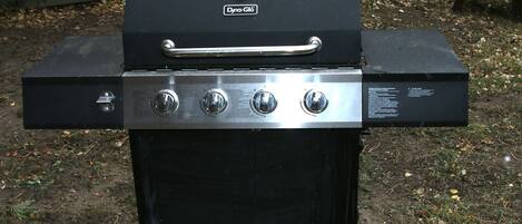 Una parrilla para exteriores negra con un asa y cuatro perillas de control.