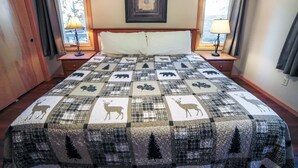 Un dormitorio con una cama grande, dos mesitas de noche con lámparas, un cuadro enmarcado en la pared y una ventana con cortinas.