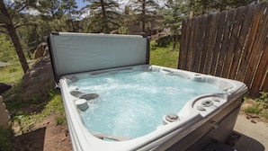 Un jacuzzi en un entorno exterior con valla de madera y árboles al fondo.