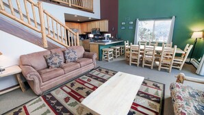 A spacious living room with a high wooden staircase, a kitchen area, and a dining set. - Lazy R Cottages: 16a 2 Bedroom Cabin (Estes Park)