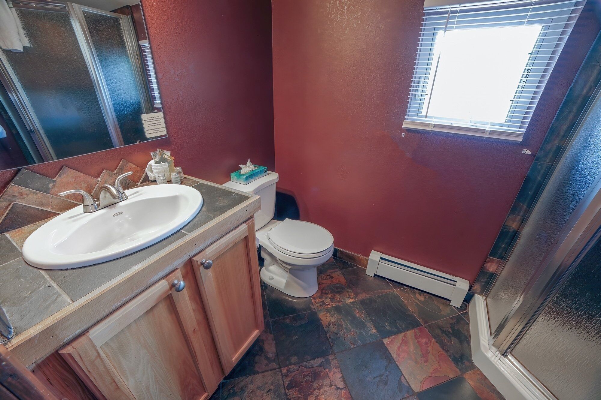 A bathroom with a white sink, toilet, and a window with blinds.