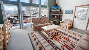A spacious living room with a large window, a fireplace, and a cozy seating area. - Lazy R Cottages: 16a 2 Bedroom Cabin (Estes Park)