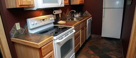 A compact kitchen with wooden cabinets, a white microwave, a stove, and a refrigerator.