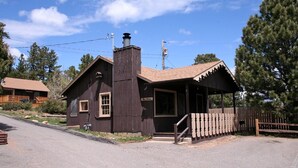 Um edifício rústico de madeira com chaminé, varanda e área cercada.