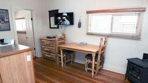 A cozy room with a wooden dining table, chairs, a TV mounted on the wall, and a wood stove. - Triple R Cottages: 2 1 Bedroom Cabin (Estes Park)