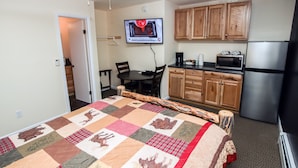 A compact hotel room with a bed, a small dining table, a kitchenette, and a TV mounted on the wall. - Fawn Valley Inn: 294 1 Bedroom Condo (Estes Park)