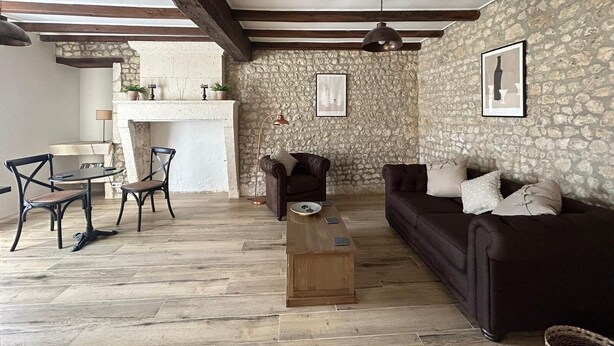 Ein rustikales Wohnzimmer mit freiliegenden Holzbalken, Steinwänden, einem Kamin und einer gemütlichen Sitzecke.
