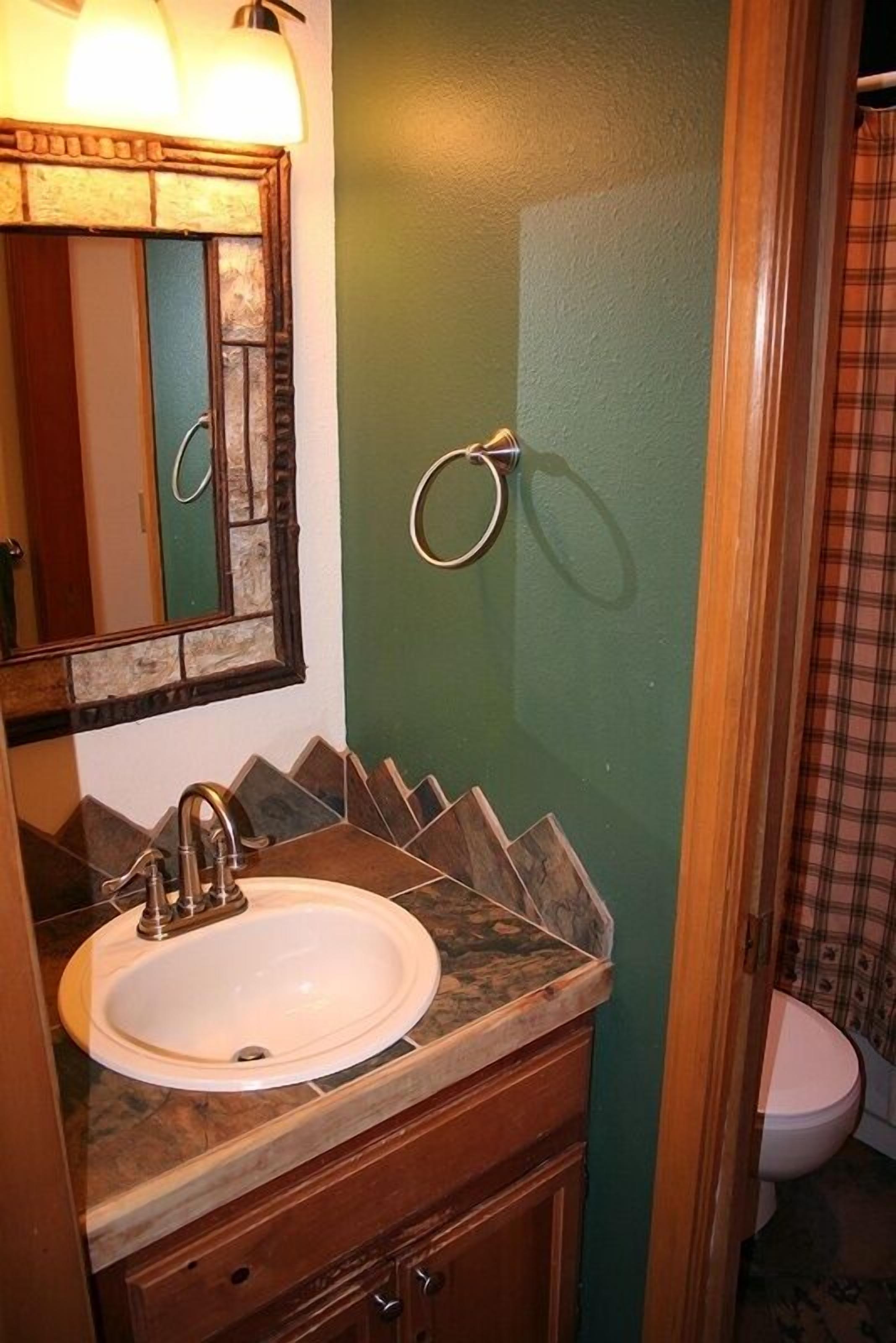 Une salle de bain avec un lavabo blanc, un miroir avec un cadre en bois et un mur vert.