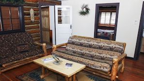 A log cabin interior with a rustic wooden sofa, a wooden coffee table, and a patterned rug. - Triple R Cottages: 1 3 Bedroom Cabin (Estes Park)