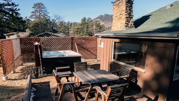 An outdoor patio with wooden furniture, a hot tub, and a stone chimney. - Triple R Cottages: 1 3 Bedroom Cabin (Estes Park)