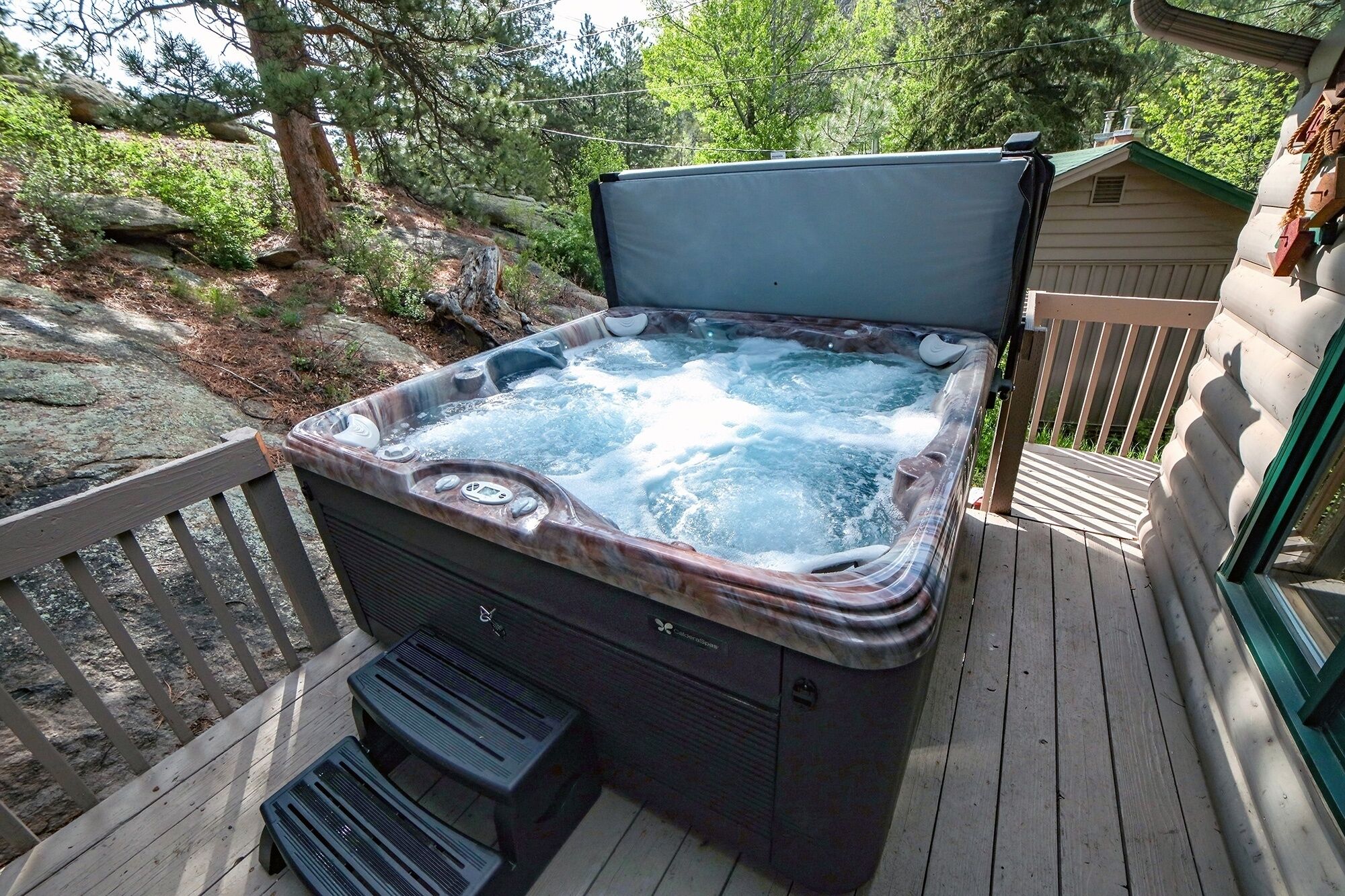 Un jacuzzi en una terraza de madera con cercado de madera y árboles al fondo.