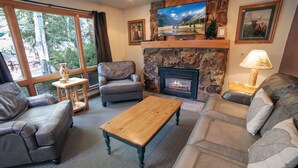 A cozy living room with leather sofas, a wooden coffee table, a stone fireplace, and a television mounted on a stone wall. - Sunnyside Knoll: 7 1 Bedroom Cabin (Estes Park)