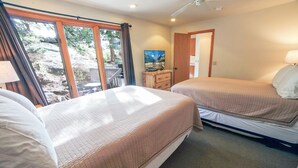 A hotel room with two beds, a TV, a dresser, and a window with a view of trees and a deck. - Sunnyside Knoll: 7 1 Bedroom Cabin (Estes Park)