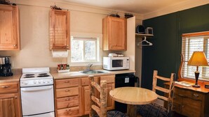 A compact kitchen with wooden cabinets, a stove, a microwave, a sink, and a small dining table with chairs. - Triple R Cottages: 4 1 Bedroom Cabin (Estes Park)