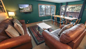 A cozy living room with leather sofas, a coffee table, and a TV mounted on the wall displaying a scenic view. - Timber Creek Chalets: 14 3 Bedroom Chalet (Estes Park)