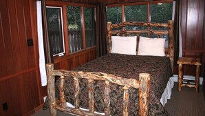 A wooden-paneled bedroom with a bed featuring a rustic headboard, large windows, and a small wooden stool. - Timber Creek Chalets: 14 3 Bedroom Chalet (Estes Park)