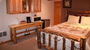A bedroom with a wooden bed frame, a wooden nightstand with a microwave, and a wooden wardrobe. - Fawn Valley Inn: 253 1 Bedroom Apts (Estes Park)