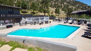 A swimming pool with lounge chairs and a lifeguard tower, surrounded by a mountainous landscape. - Fawn Valley Inn: 253 1 Bedroom Apts (Estes Park)
