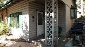 A log cabin with a porch, a lattice screen, and a barbecue grill. - Sunnyside Knoll: 8 1 Bedroom Cabin (Estes Park)