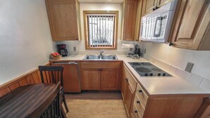 A compact kitchen with wooden cabinets, a built-in stove, a sink, and a window with bars. - Sunnyside Knoll: 8 1 Bedroom Cabin (Estes Park)
