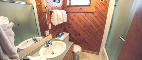 Ein Badezimmer mit Holzvertäfelung, zwei Waschbecken, einer Toilette und einem Fenster mit Jalousien.