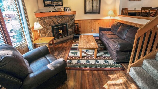 A cozy living room with a fireplace, leather sofa, and a television mounted on the wall. - Sunnyside Knoll: 8 1 Bedroom Cabin (Estes Park)
