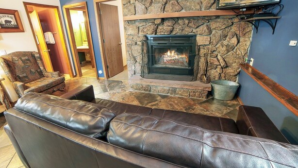 Una sala de estar con chimenea de piedra, sofá de cuero y televisor montado en la pared.