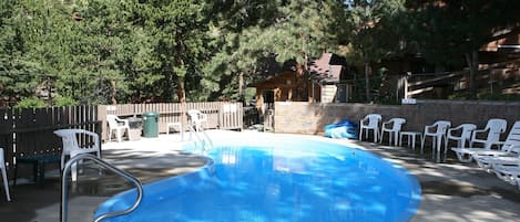 Una piscina con tabla de clavados, rodeada de sillas de plástico blancas y un muro de piedra.