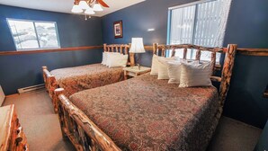 Un dormitorio con dos camas, cabeceros de madera, una mesita de noche, una lámpara y un ventanal con persianas.
