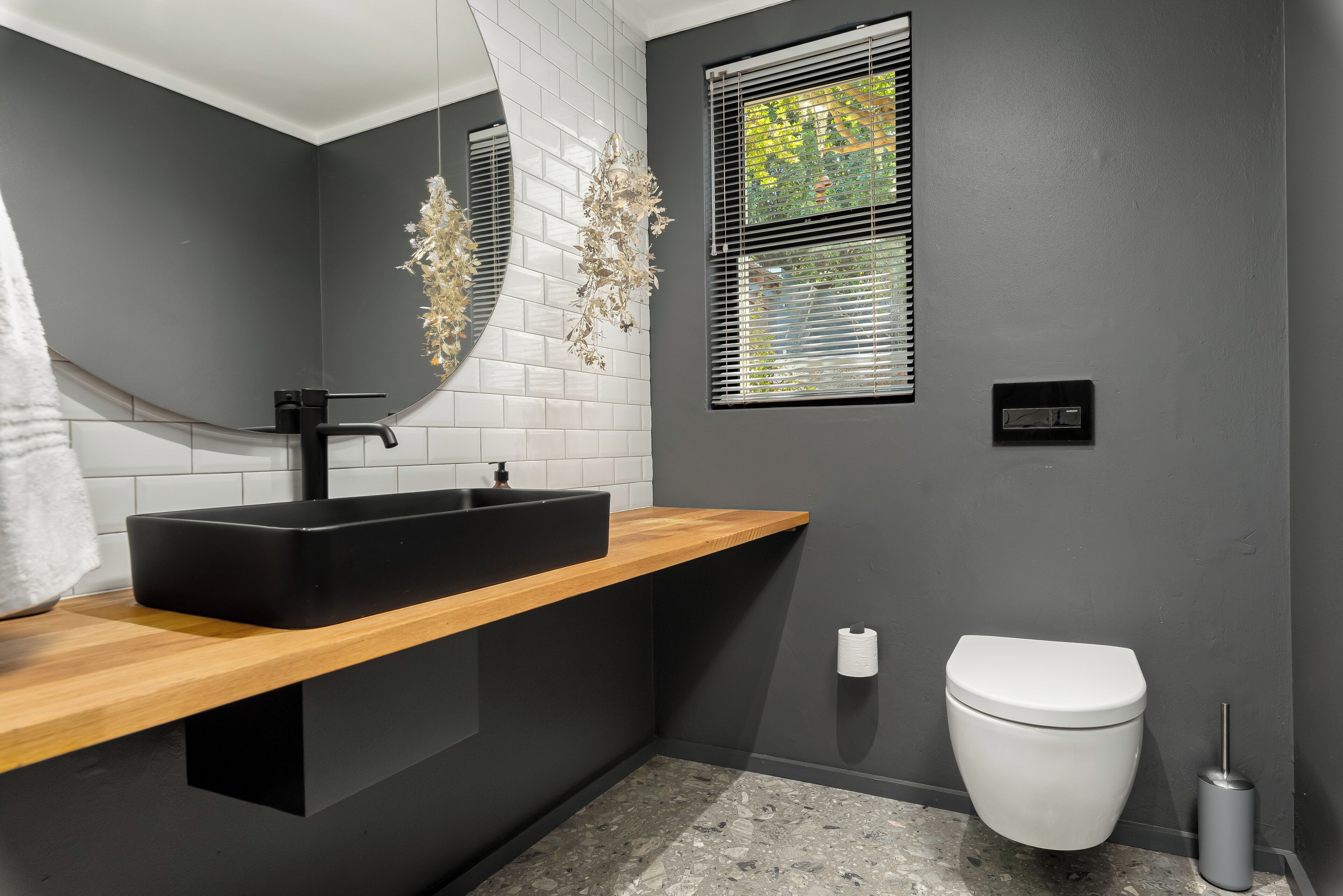 A modern bathroom with a black sink, wooden countertop, white toilet, and a mirror with decorative elements.