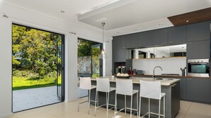 Eine moderne Küche mit einer großen Kochinsel, Barhocker und Blick auf einen grünen Garten durch eine Schiebetür.