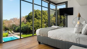 Ein Schlafzimmer mit großem Fenster, einem Bett, einem Fernseher und einer Pendelleuchte.