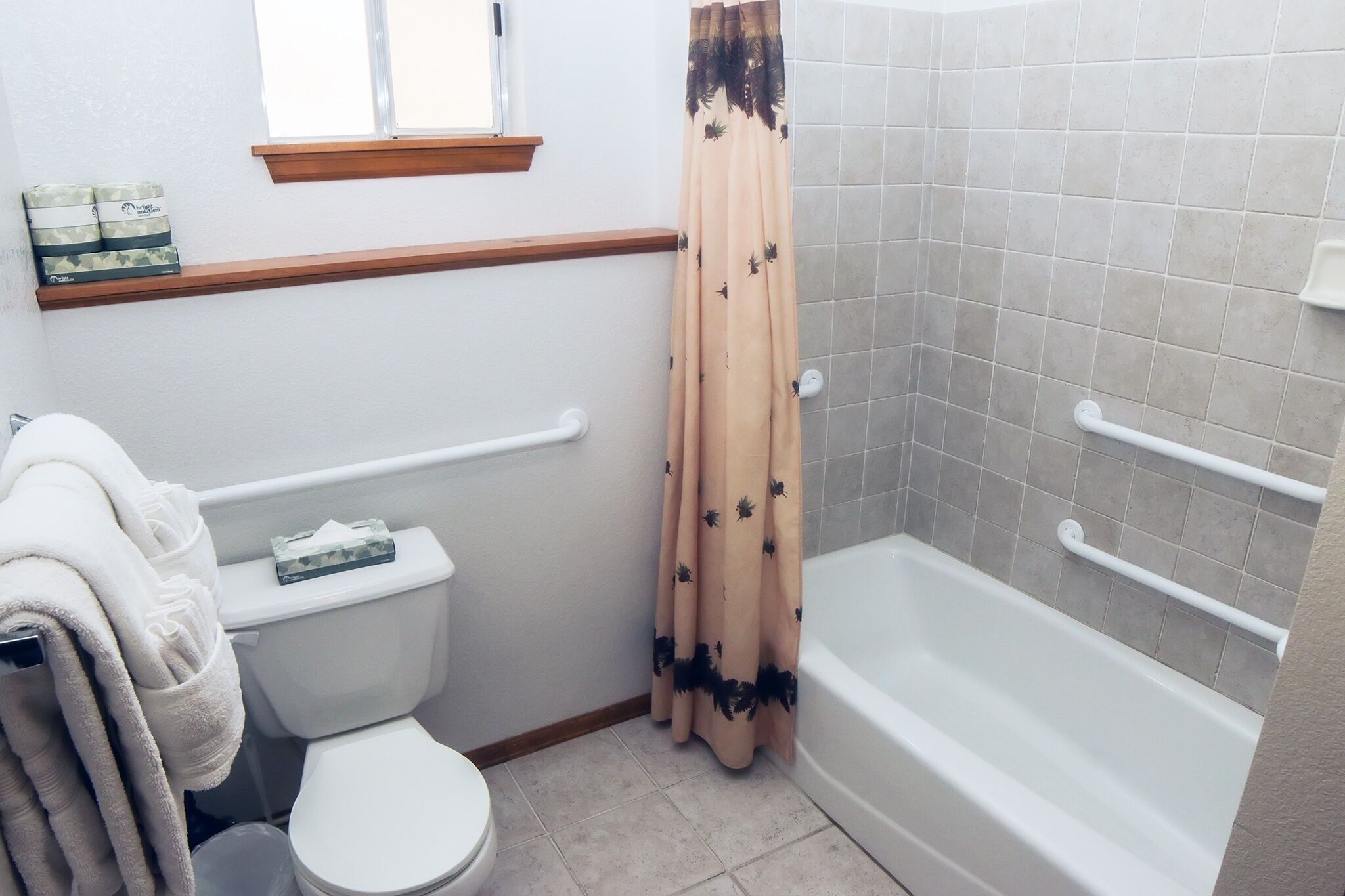 A bathroom with a toilet, a bathtub with handrails, a shower curtain, and a window above the toilet.