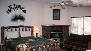 A room with a bed, a wooden headboard, a fireplace, a sofa, and a ceiling fan. - Timber Creek Chalets: 11 1 Bedroom Chalet (Estes Park)