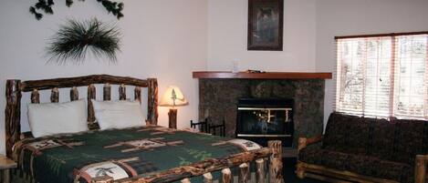 A room with a bed, a wooden headboard, a fireplace, a sofa, and a ceiling fan.