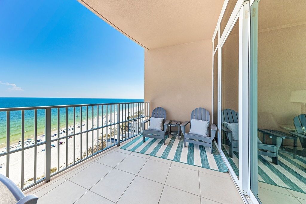 A balcony with two chairs and a small table, overlooking a beach and the ocean.