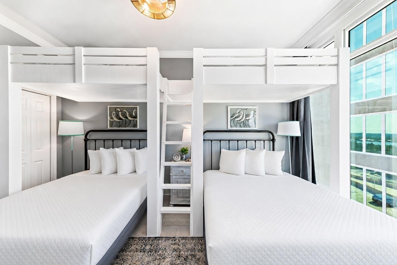 Habitación de hotel con dos camas, un pasillo central, obras de arte, vistas a través de grandes ventanales y una lámpara de techo moderna.