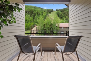 A balcony with two chairs, a view of a green valley, and a house in the background.