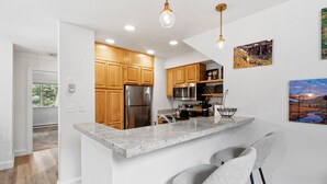 A modern kitchen with wooden cabinets, stainless steel appliances, a granite countertop, and two bar stools.