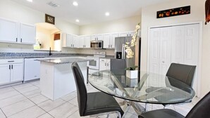 A modern kitchen with white cabinets, a glass dining table, and black chairs. - Golden Beach Villa 6 Bedroom Home by RedAwning (Kissimmee)
