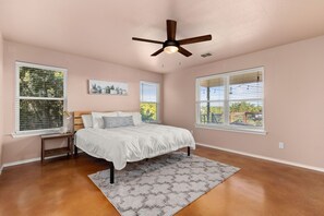 A bedroom with a bed, a ceiling fan, a nightstand, a rug, and two windows with blinds.